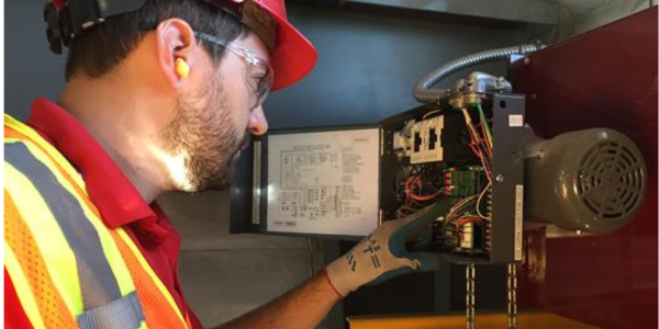  Cornell certified technician in a hard hat performing maintenance on the motor of a commercial rolling door.
