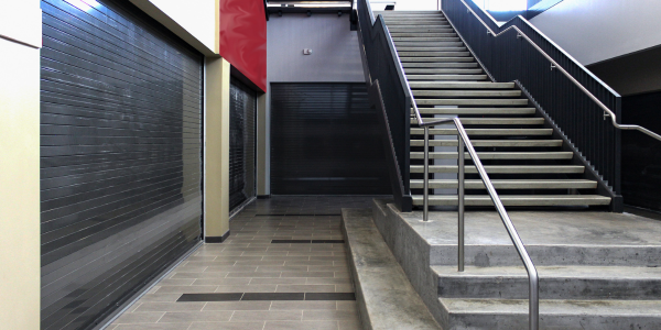 An automatically closing rolling steel fire door, shown partially descended in a building corridor during a fire event.
