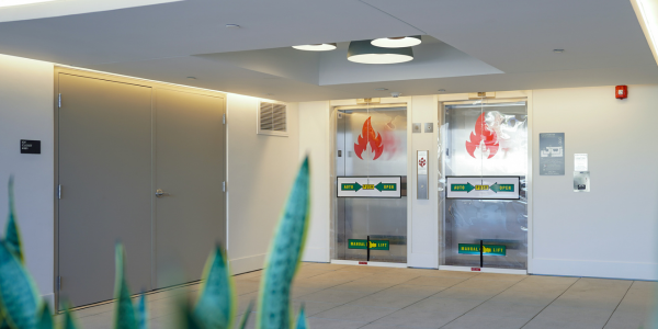A fabric smoke and fire curtain, the Cornell SmokeShield, is shown deploying from the ceiling to seal off a hallway for safety.